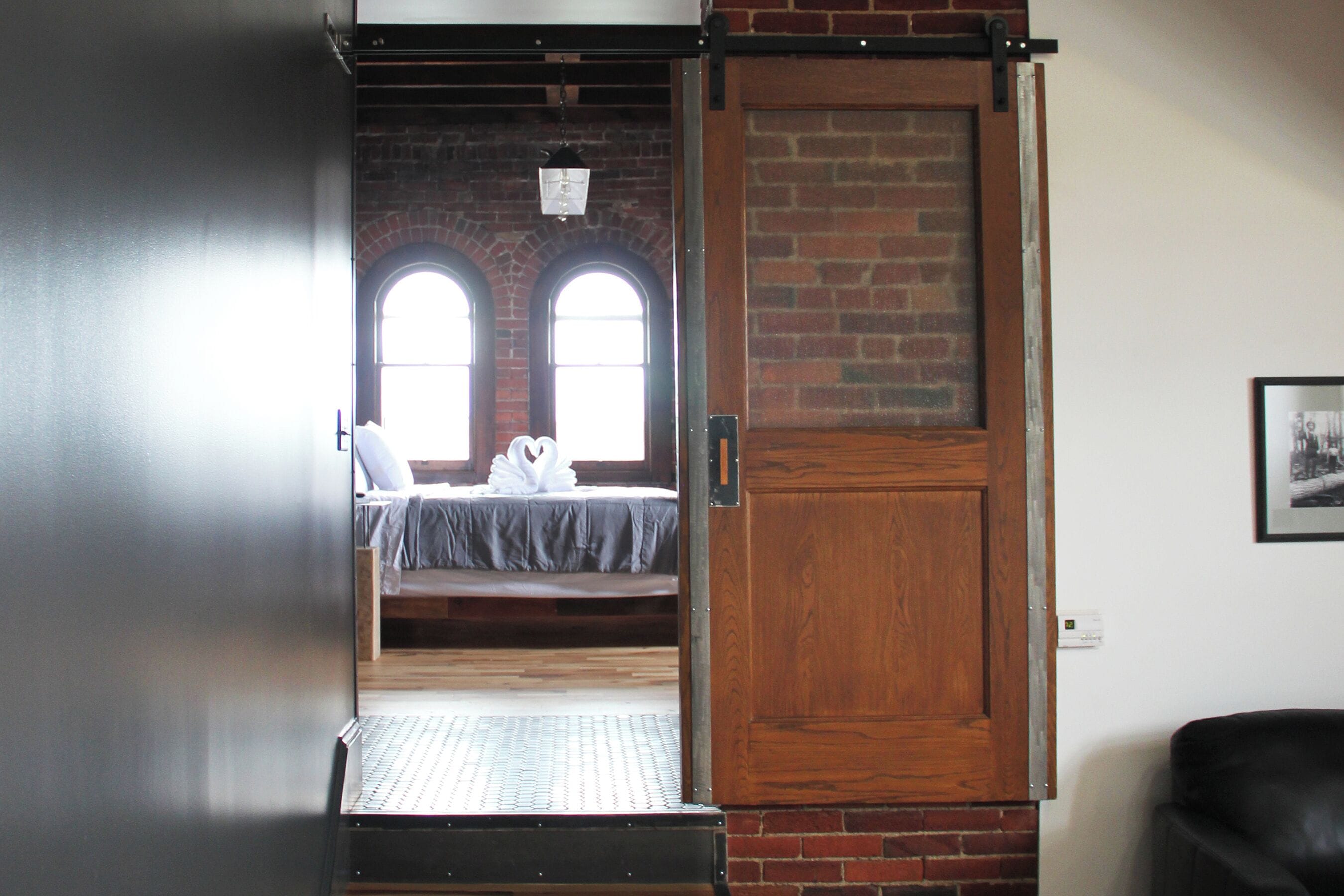 A room with a bed, a wooden door, and a brick wall.