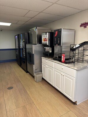 A commercial kitchen with stainless steel appliances, a beverage dispenser, and a trash can. - Econo Lodge Waite Park - St. Cloud (Waite Park)