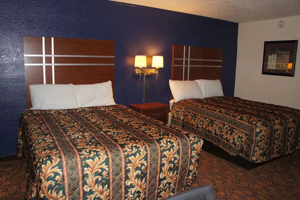 A hotel room with two beds, a nightstand, and a wall-mounted lamp.