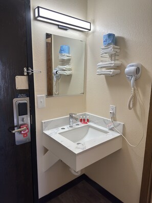 A hotel bathroom with a white sink, a mirror, a hairdryer, and a towel rack. - Econo Lodge Waite Park - St. Cloud (Waite Park)