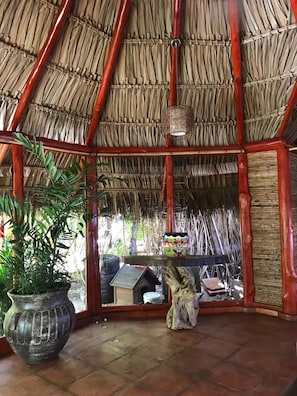 Una habitación con techo de paja, una planta grande en maceta y una escultura de madera.