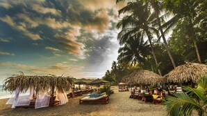 A beach with thatched umbrellas, wooden lounge chairs, and a sandy beach. - Hotel Locanda Samara Beach (Sámara)