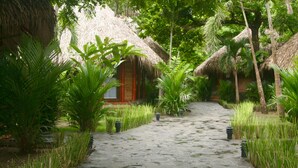 A stone pathway leading to a thatched-roof structure surrounded by lush greenery. - Hotel Locanda Samara Beach (Sámara)