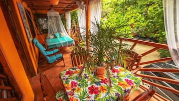 Un balcon avec une table recouverte d’une nappe à motifs floraux, entourée de plantes en pot et agrémenté d’une chaise bleue.