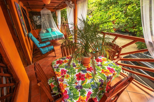 A balcony with a table covered in a floral tablecloth, surrounded by potted plants and a blue chair. - Hotel Locanda Samara Beach (Sámara)