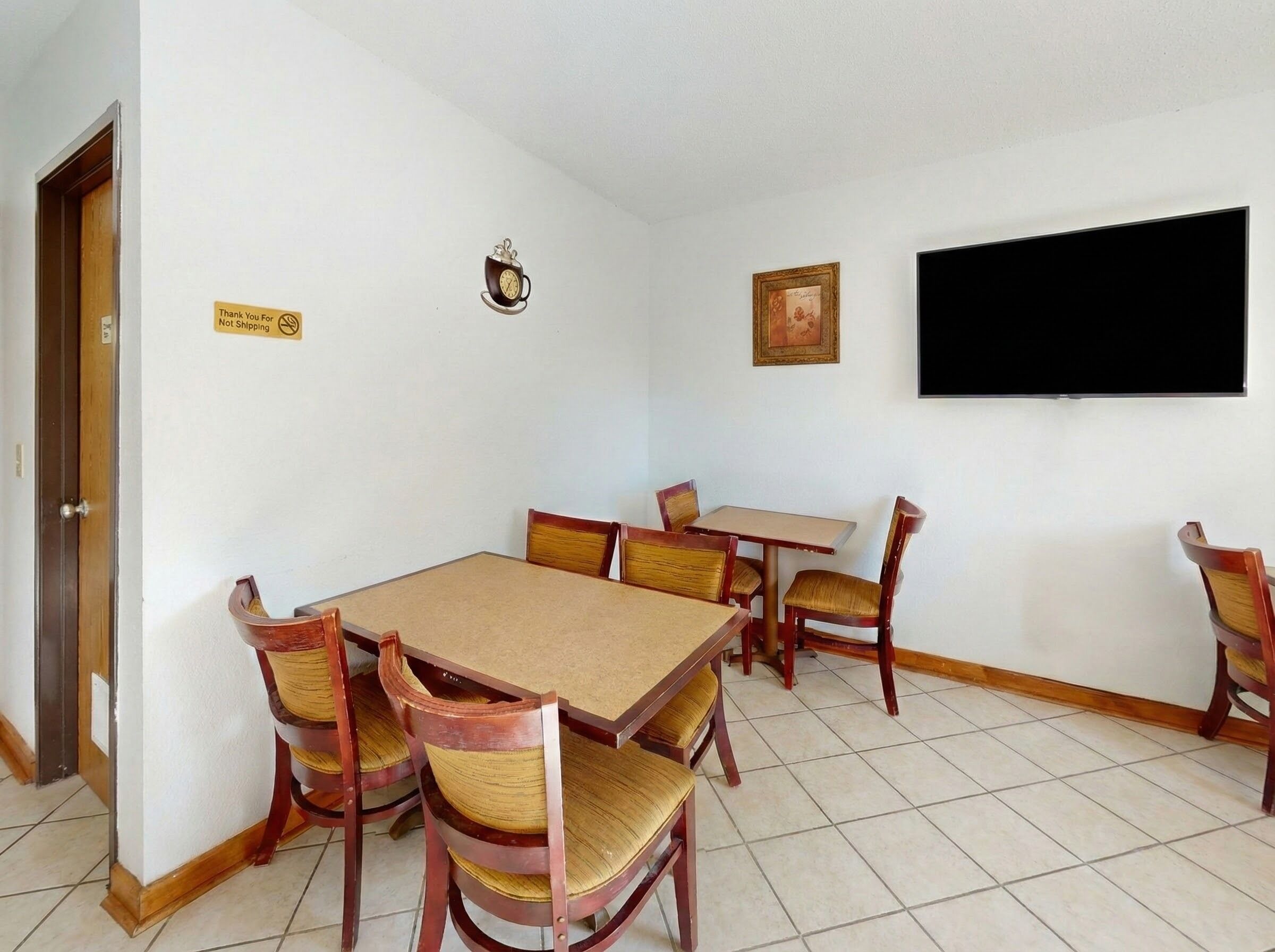 A dining area with a wooden table and chairs, a clock, a television, and a 'Not Shipping' sign.