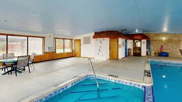 An indoor swimming pool with clear blue water, a pool ladder, and a tiled edge. There is a wooden door and a small room with a window.