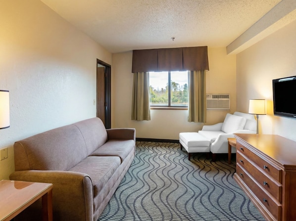 Ein Hotelzimmer mit einem braunen Sofa, einem weißen Sessel, einem Holzschrank und einem Fernseher.