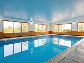 Una amplia piscina interior con paneles de madera y ventanas grandes.