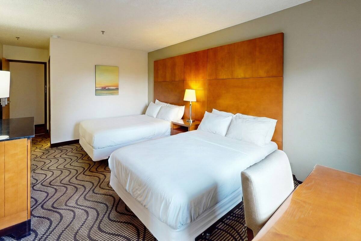 A hotel room with two beds, a desk, a chair, a lamp, and a painting on the wall.