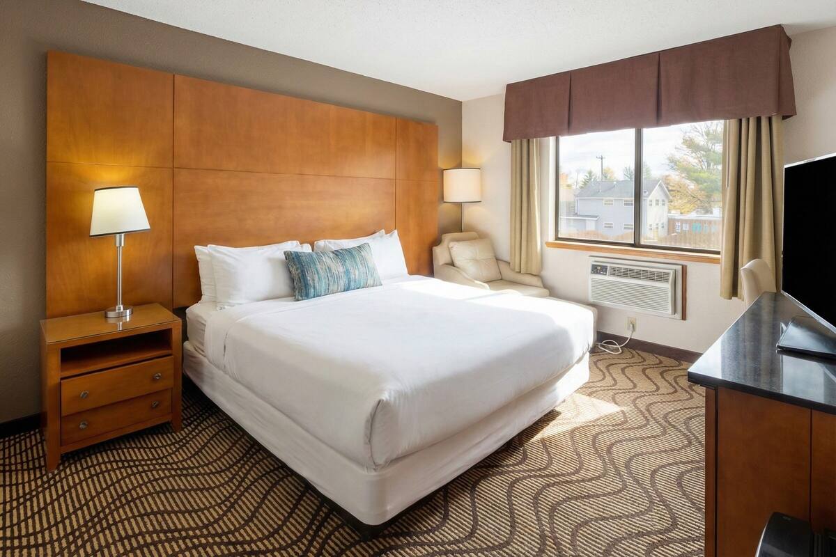 A hotel room with a large bed, a desk, a chair, a TV, and a window with curtains.