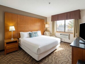 A hotel room with a large bed, a desk, a chair, a TV, and a window with curtains. - Oscoda Lakeside Hotel (Oscoda)