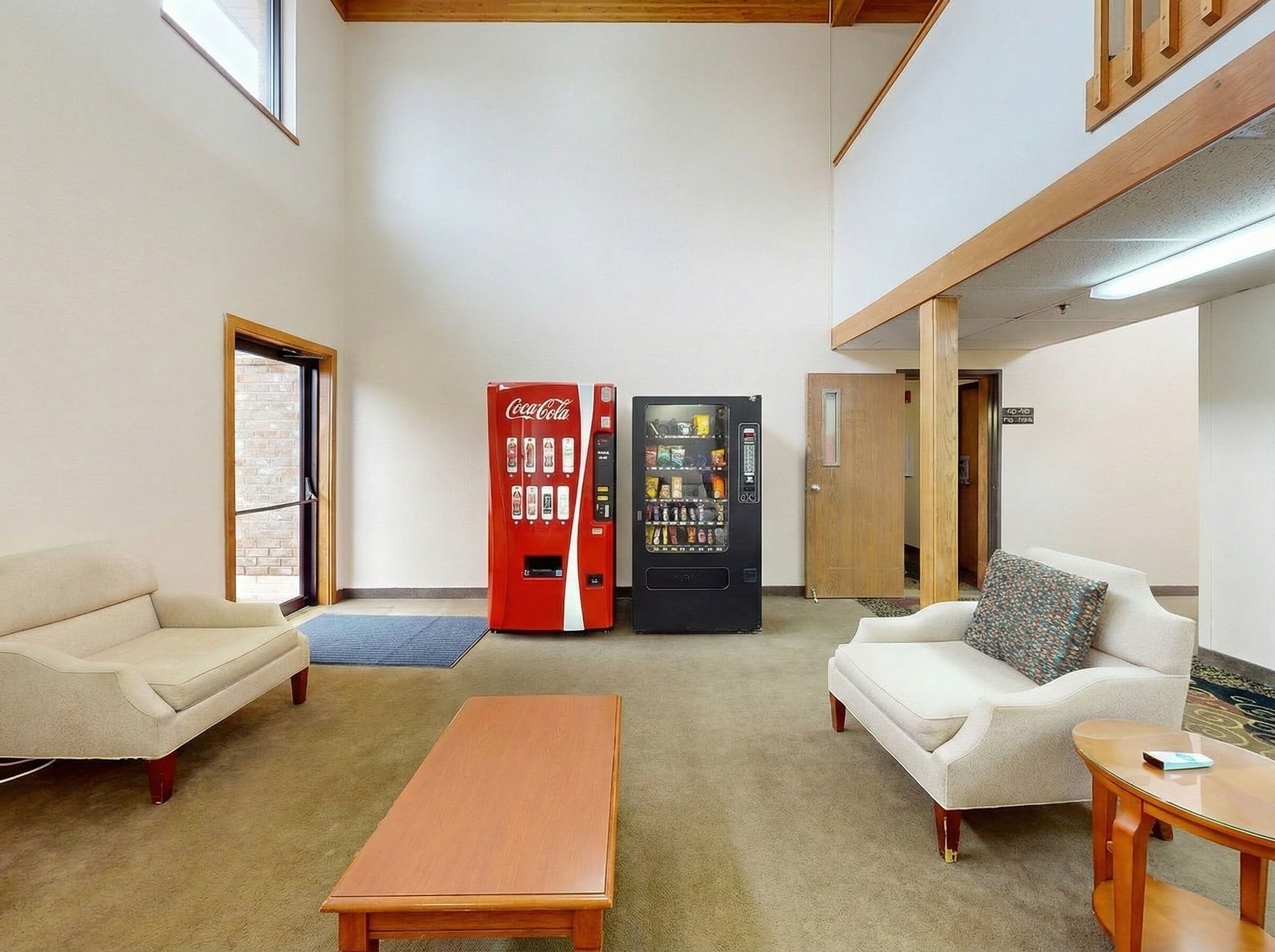 A spacious lobby with two vending machines, a sofa, a coffee table, and a door leading to another room.