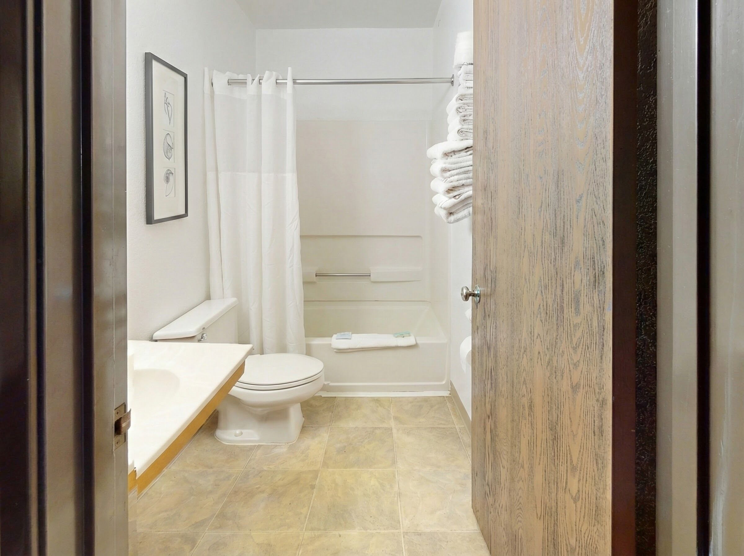 A bathroom with a toilet, a shower with a curtain, and a stack of towels.