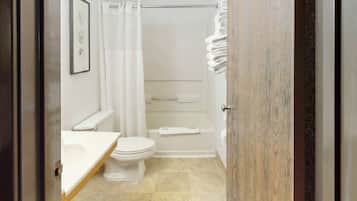 A bathroom with a toilet, a shower with a curtain, and a stack of towels.