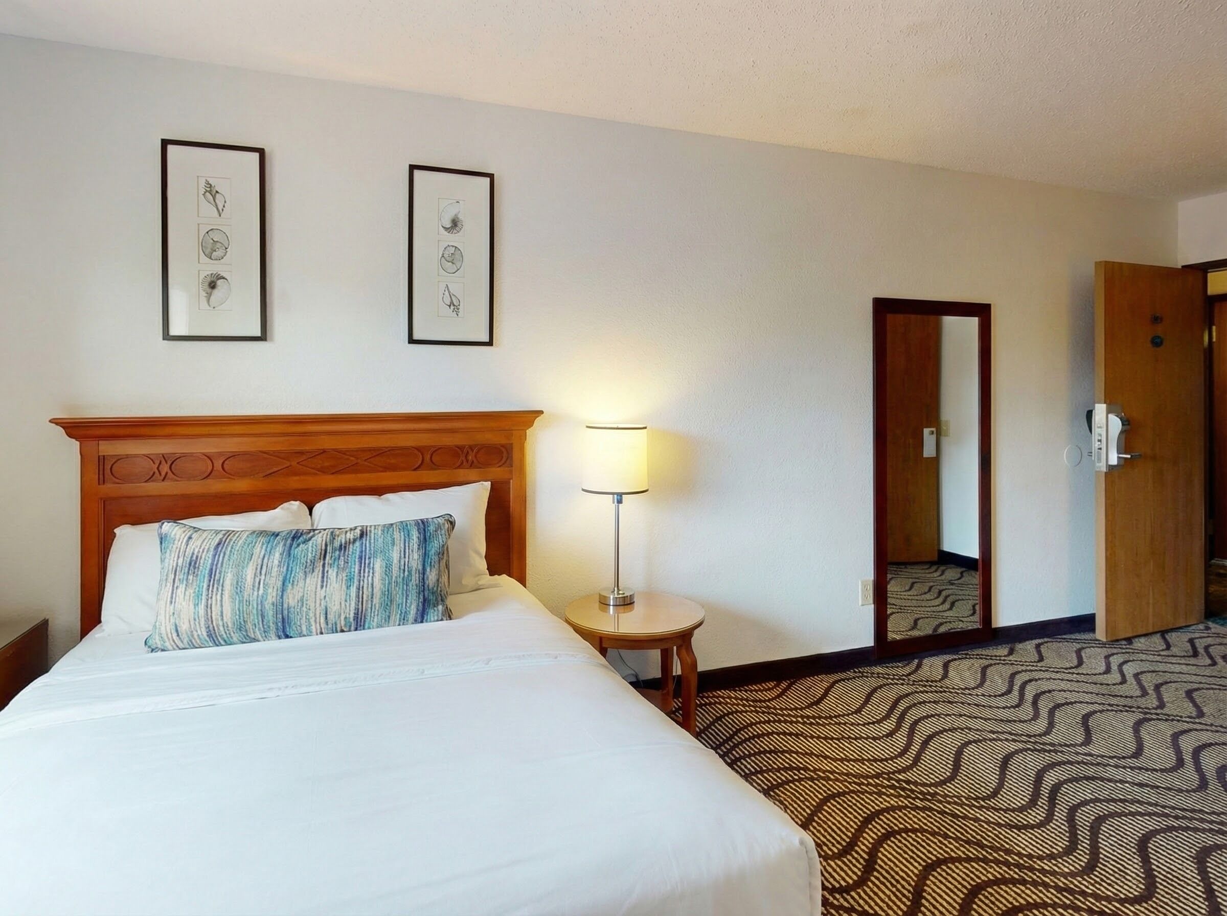 A hotel room with a bed, a nightstand, a lamp, and two framed pictures on the wall.