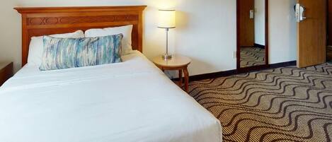 A hotel room with a bed, a nightstand, a lamp, and two framed pictures on the wall.
