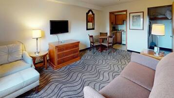 Hotelkamer met een bank, een televisie, een dressoir, een eettafel met stoelen, een keukenhoek en een kamerbreed tapijt met dessin.
