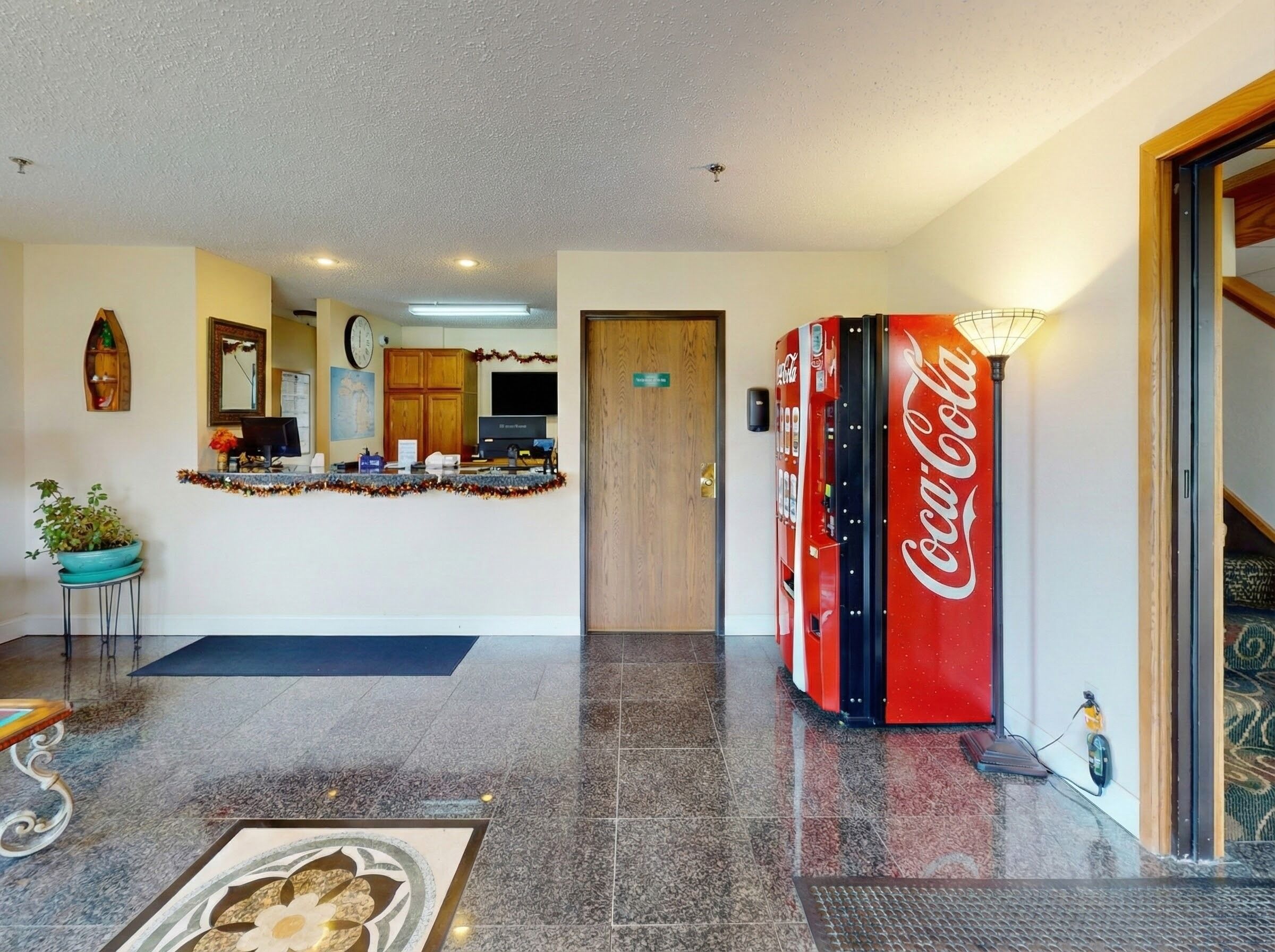 En lobby med receptionsdisk, Coca-Cola automt, et ur og en potteplante.