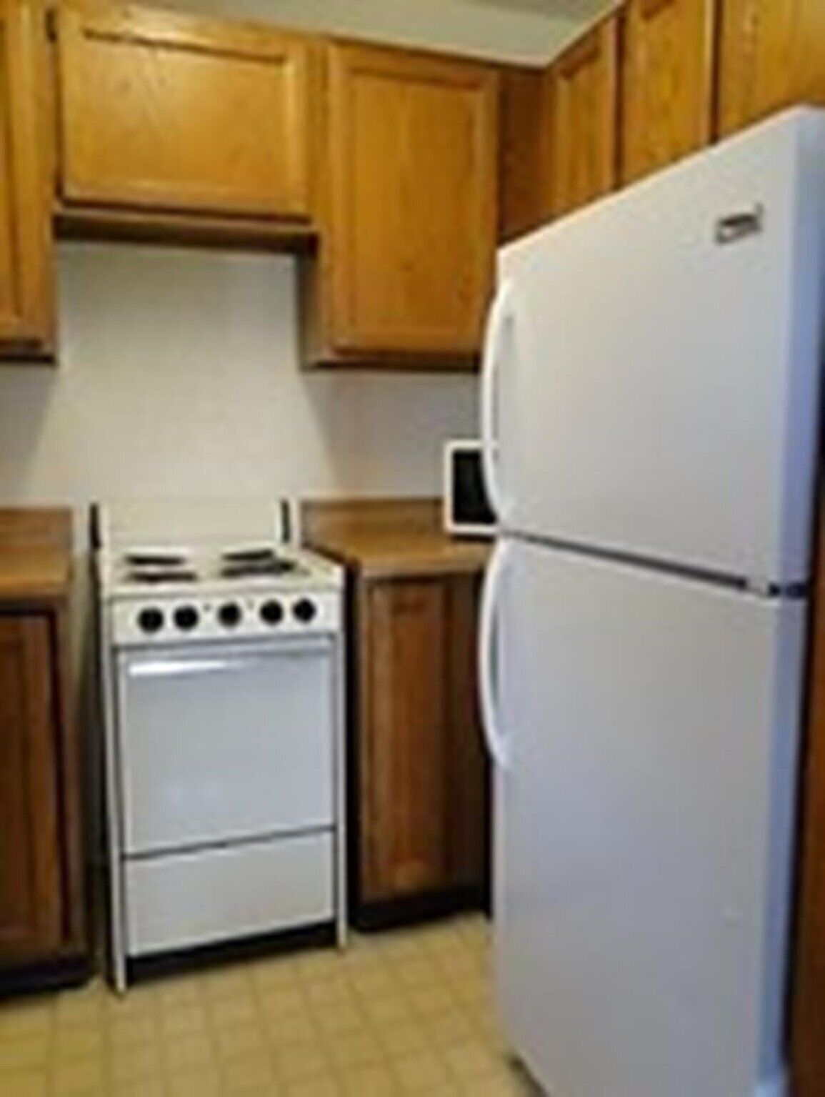 A kitchen with wooden cabinets, a white stove, and a white refrigerator.