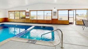Una piscina interior con vistas despejadas a la playa a través de amplios ventanales, paneles de madera y un puesto de socorristas.