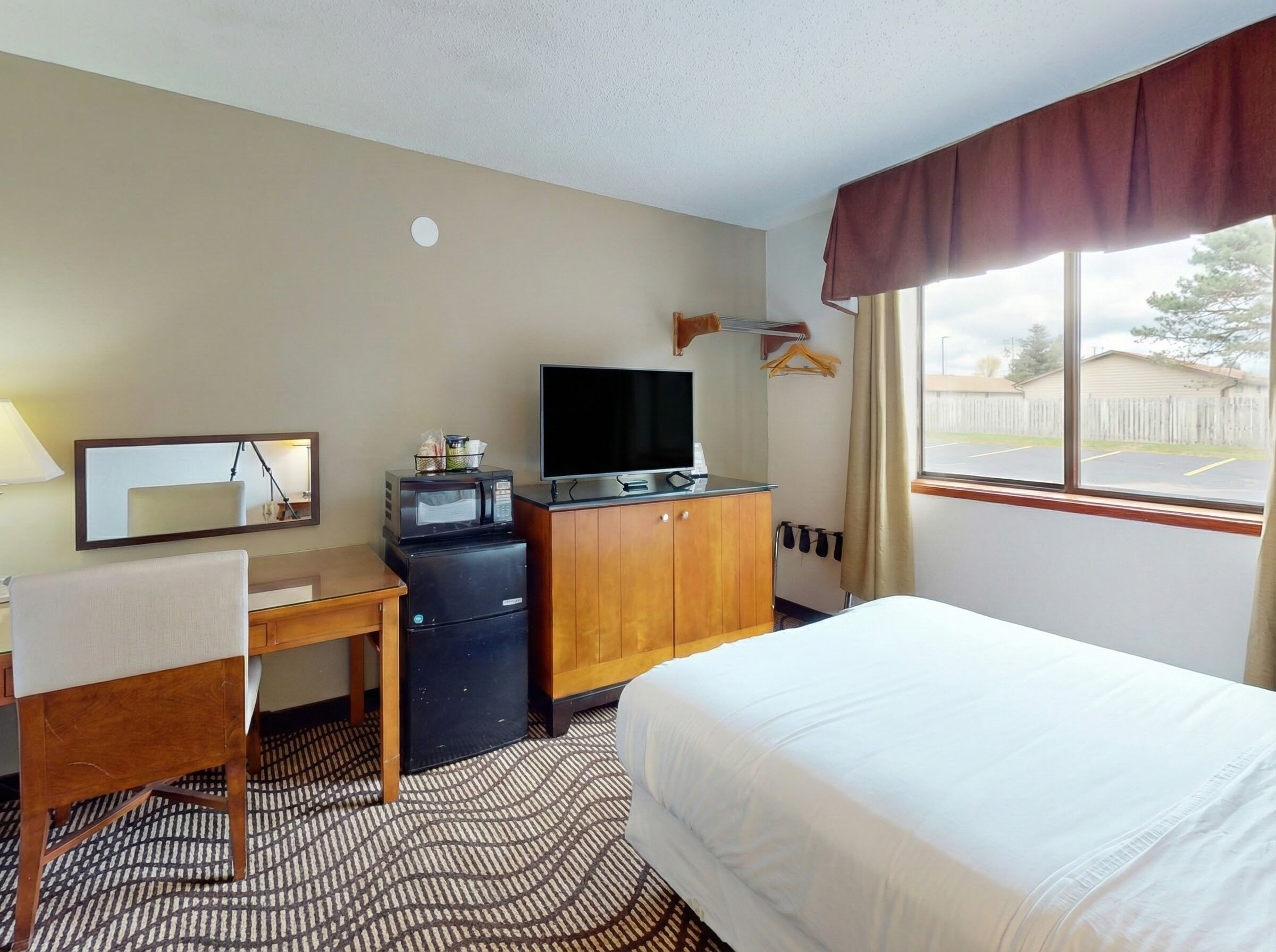 A hotel room with a bed, a desk with a chair, a TV, a microwave, and a small refrigerator.