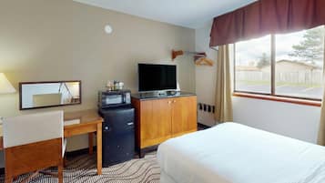 A hotel room with a bed, a desk with a chair, a TV, a microwave, and a small refrigerator.