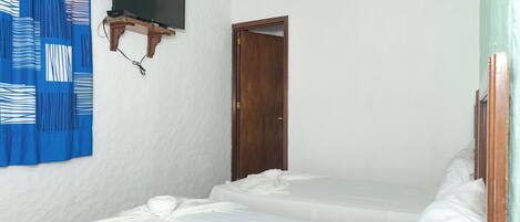 Una habitación pequeña y limpia con dos camas individuales, una puerta de madera y un televisor montado.