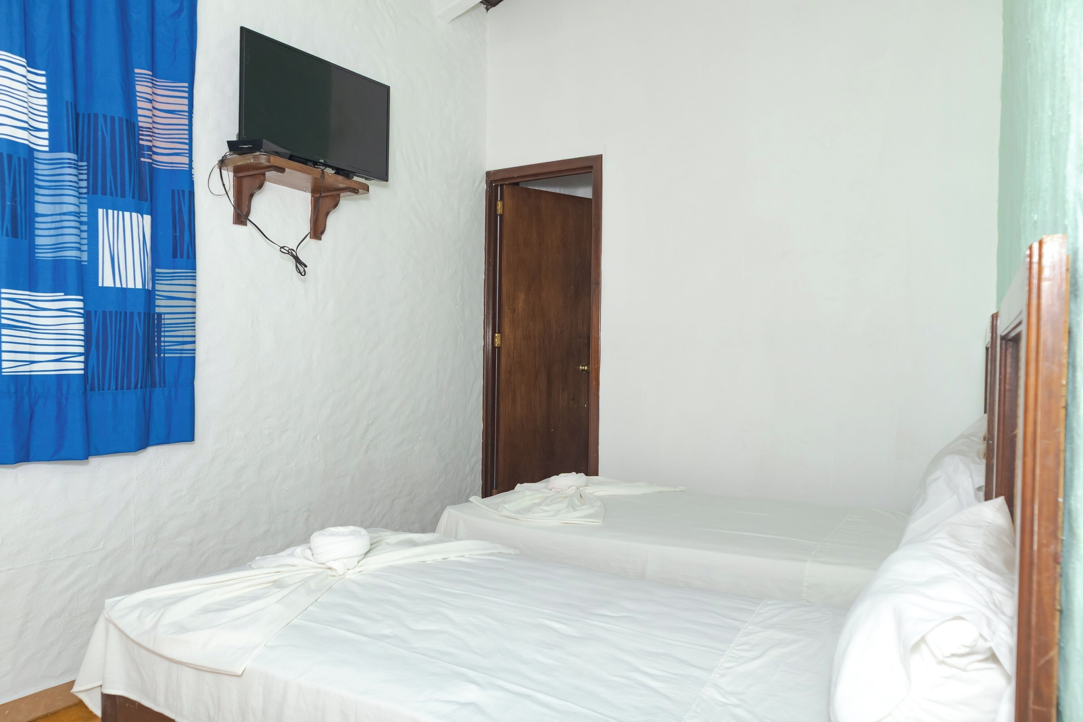 Una habitación con dos camas, un televisor instalado en la pared y una cortina azul.