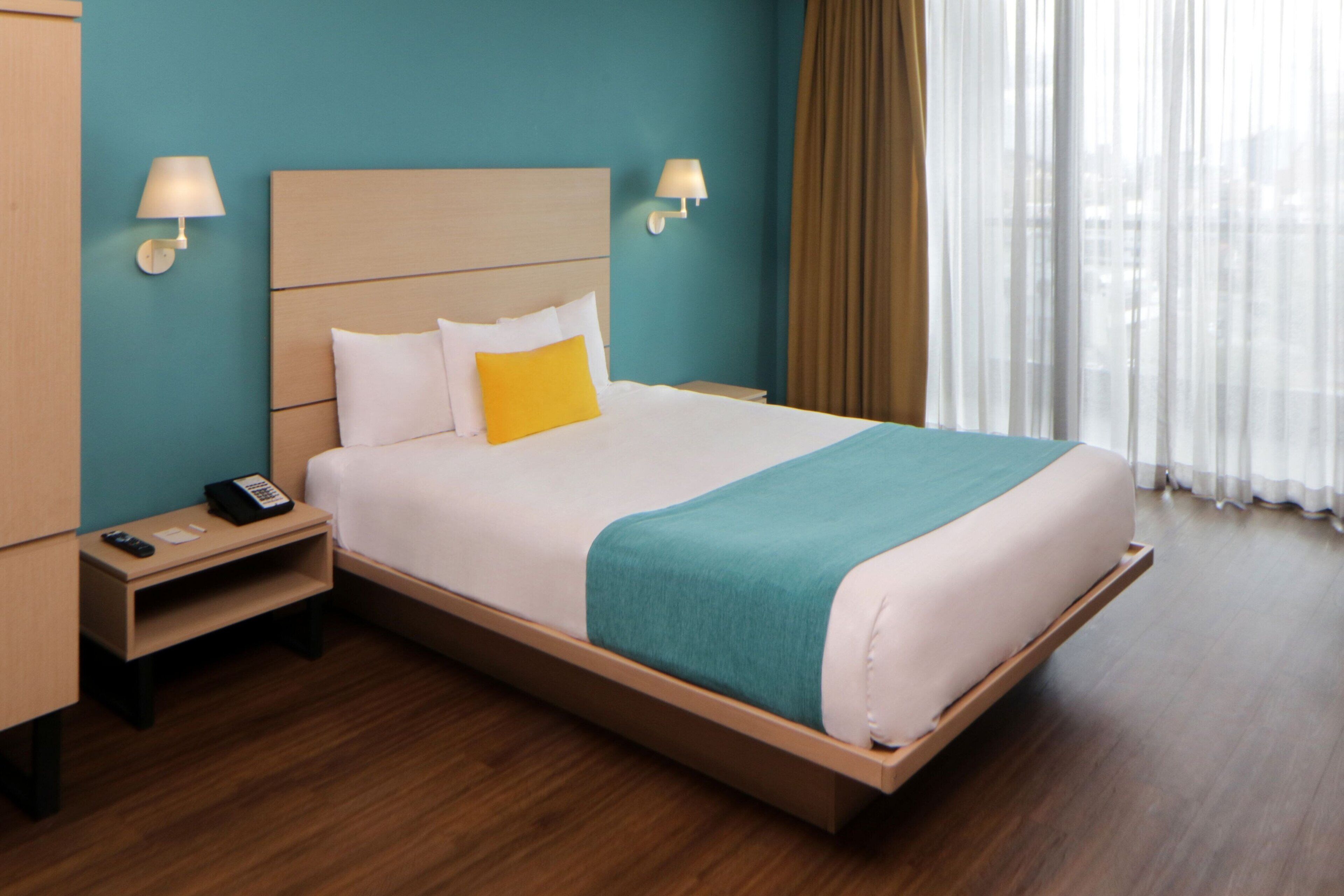 A hotel room with a bed, a nightstand, a lamp, and a window with curtains.