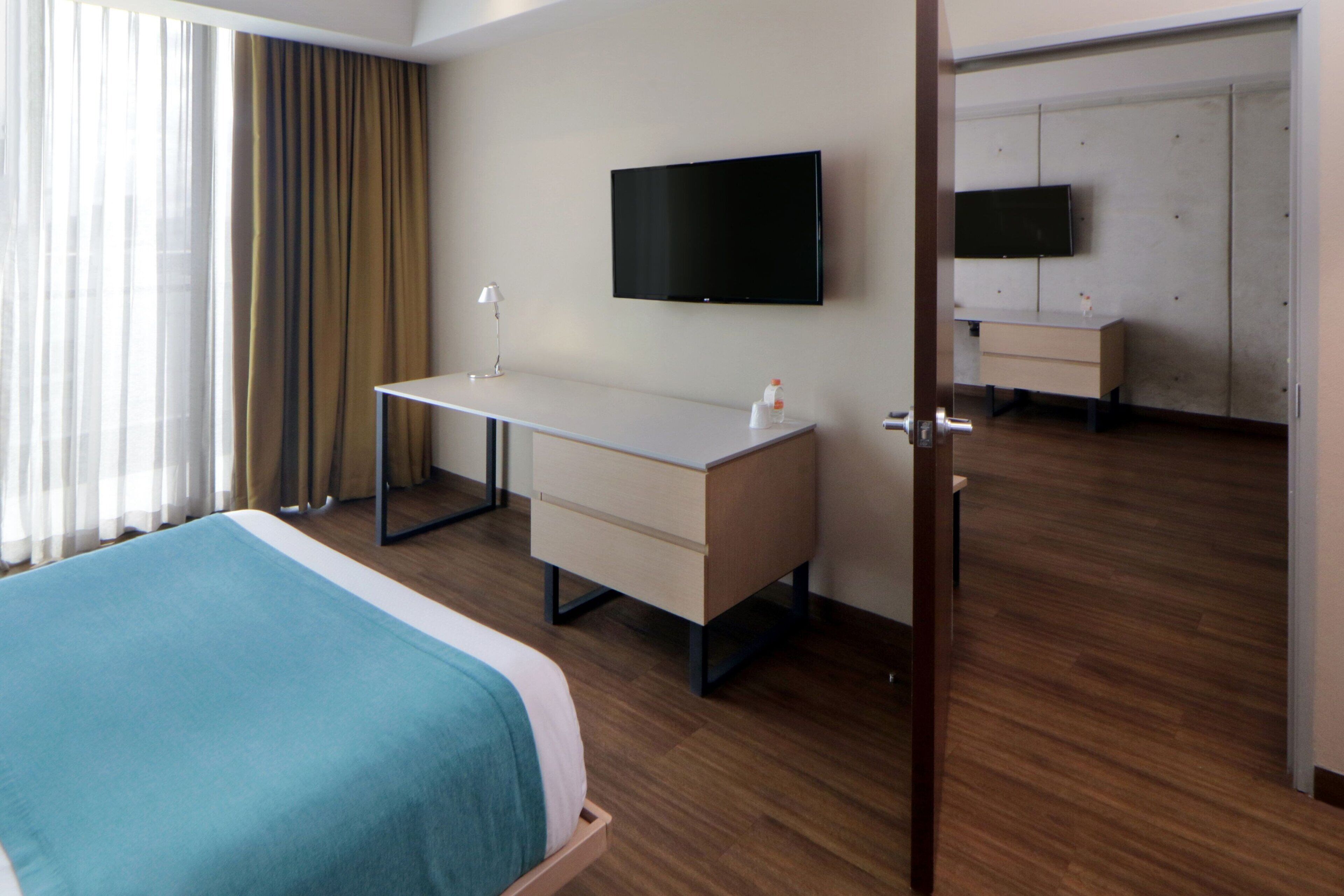 Una habitación de hotel con una cama, un escritorio, un televisor y un armario.
