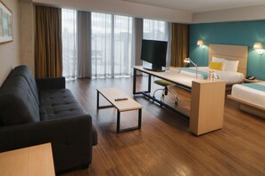 A modern hotel room with a sofa, a desk, a bed, and a television.