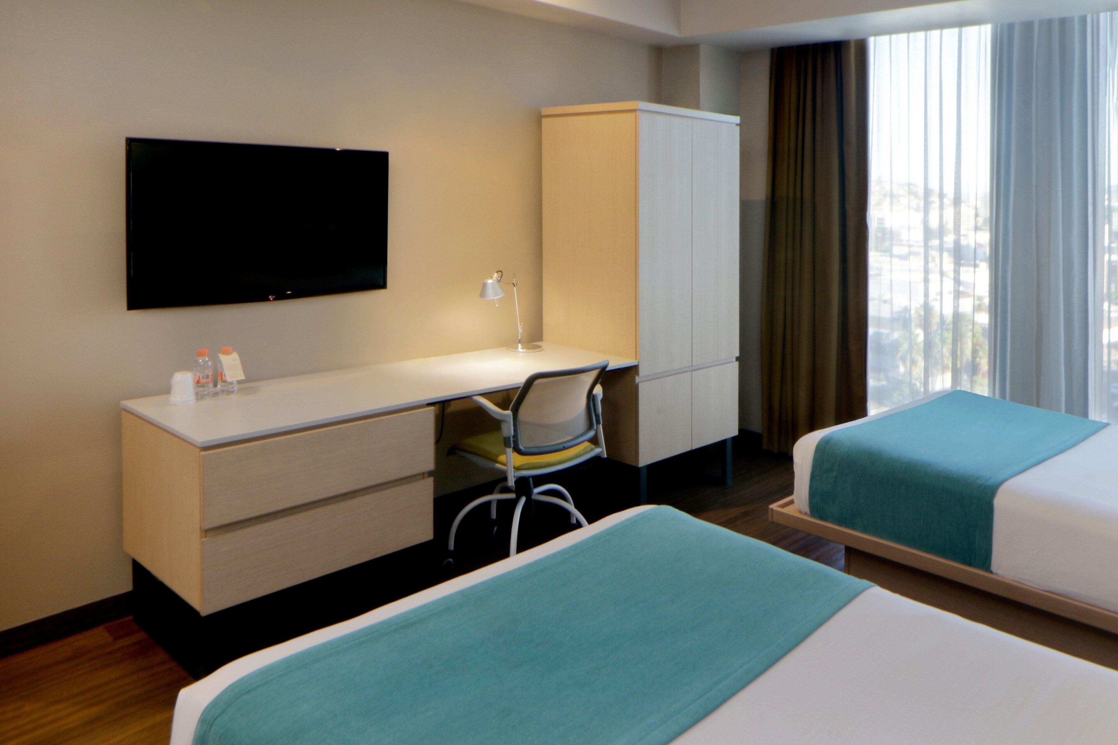 A hotel room with a bed, a desk, a chair, a TV, and a wardrobe.