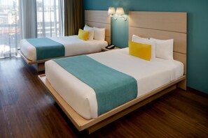 A hotel room with two beds, a wooden headboard, and a view of the city through large windows.