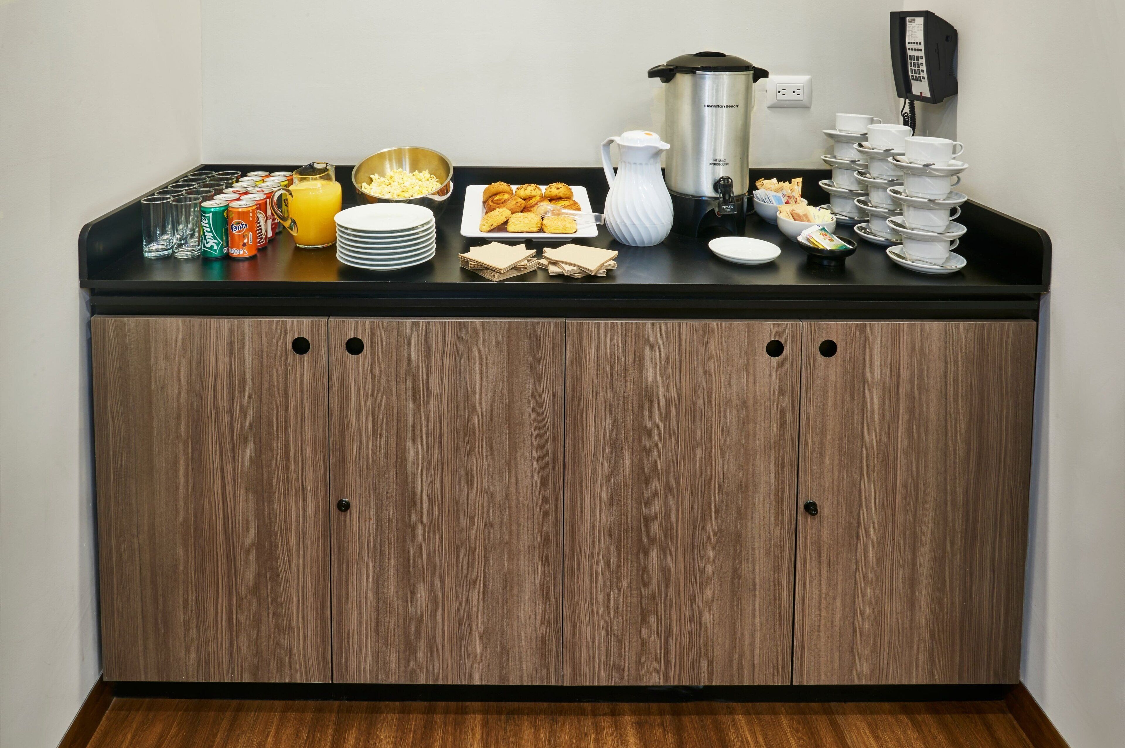 A breakfast buffet setup with various food items, a coffee maker, and a phone on the counter.