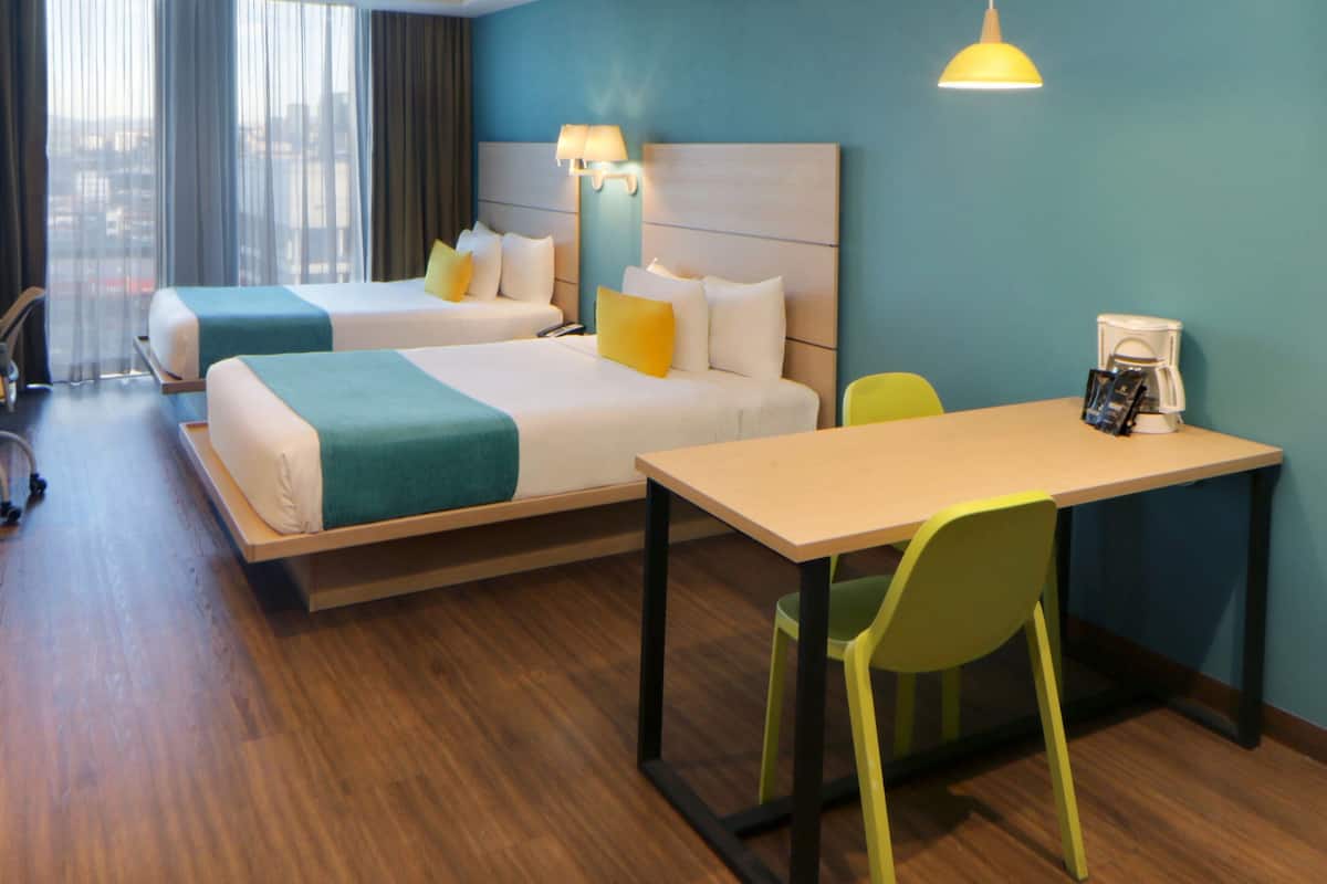 A hotel room with two beds, a desk, a chair, and a coffee maker.