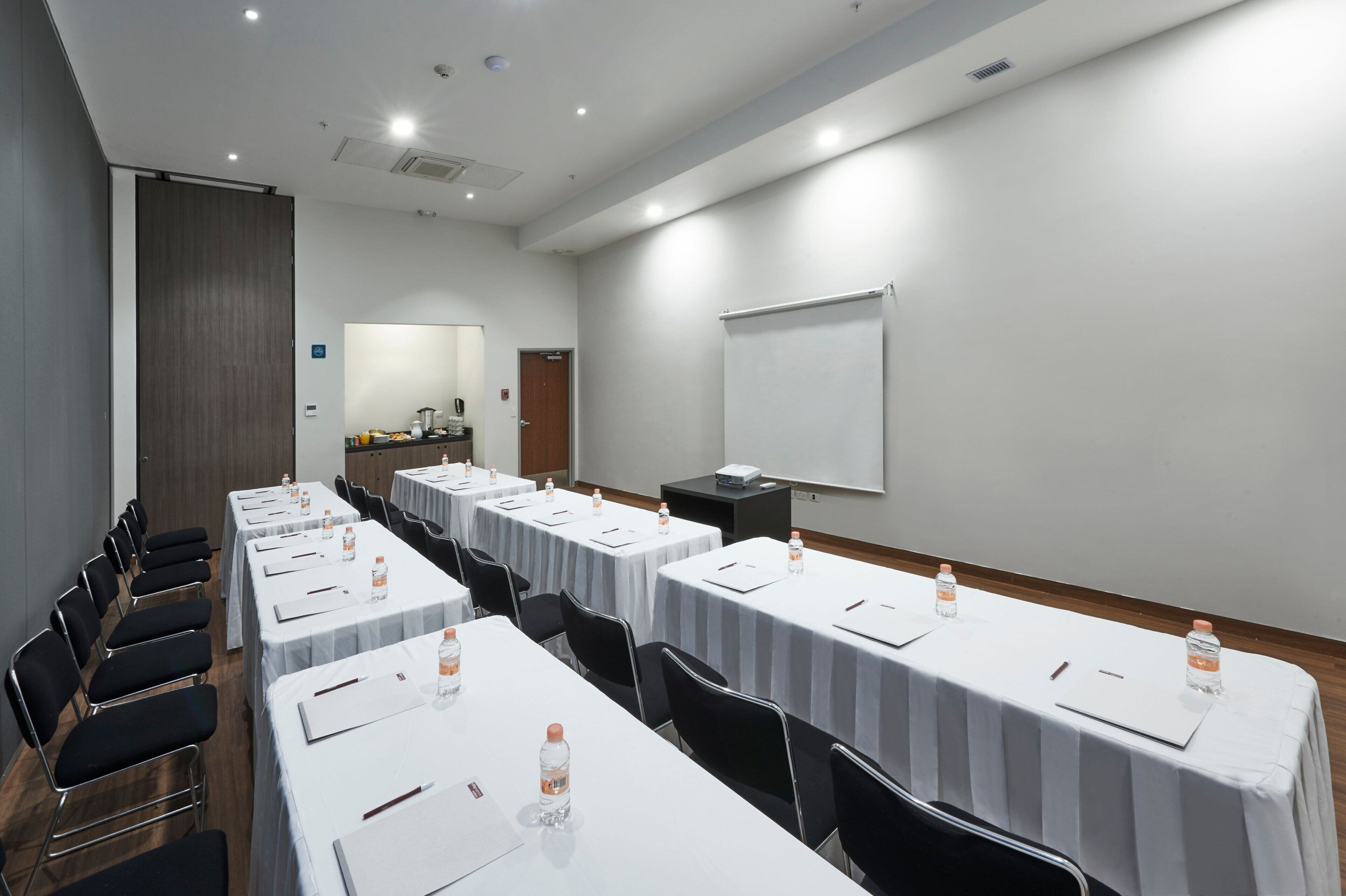 Une salle de conférence équipée de plusieurs tables, de chaises et d’un écran de projection.