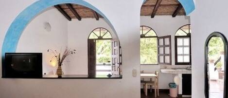 A room with a TV mounted on the wall, a vase with branches, and a window with a view of greenery.