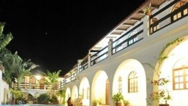 A nighttime pool area with a clear pool, arched windows, and potted plants.