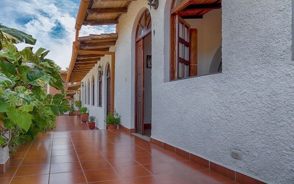 Un pasillo con paredes blancas y puertas de madera que conduce a una zona cubierta con suelo de baldosas.
