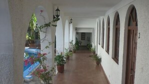 A corridor with arches, potted plants, and a pool area.