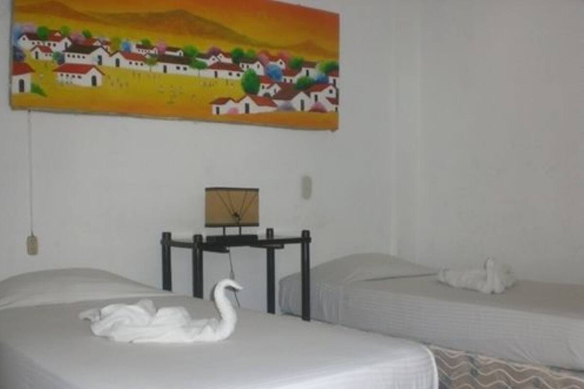 A hotel room with two beds, a painting of a village, a clock, and a small table.