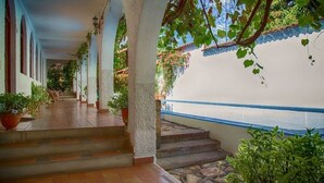 A covered outdoor area with steps leading to a pool, surrounded by potted plants and columns.