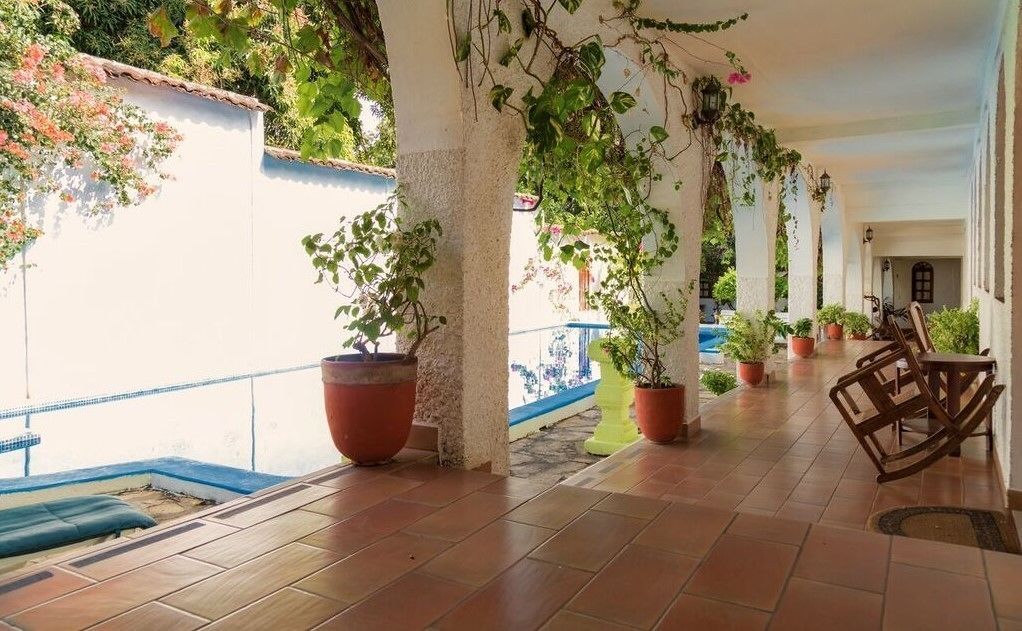 A covered outdoor area with tiled flooring, potted plants, and a seating area with a chair and table.