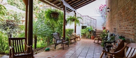 An outdoor patio with tiled flooring, wooden rocking chairs, and potted plants.