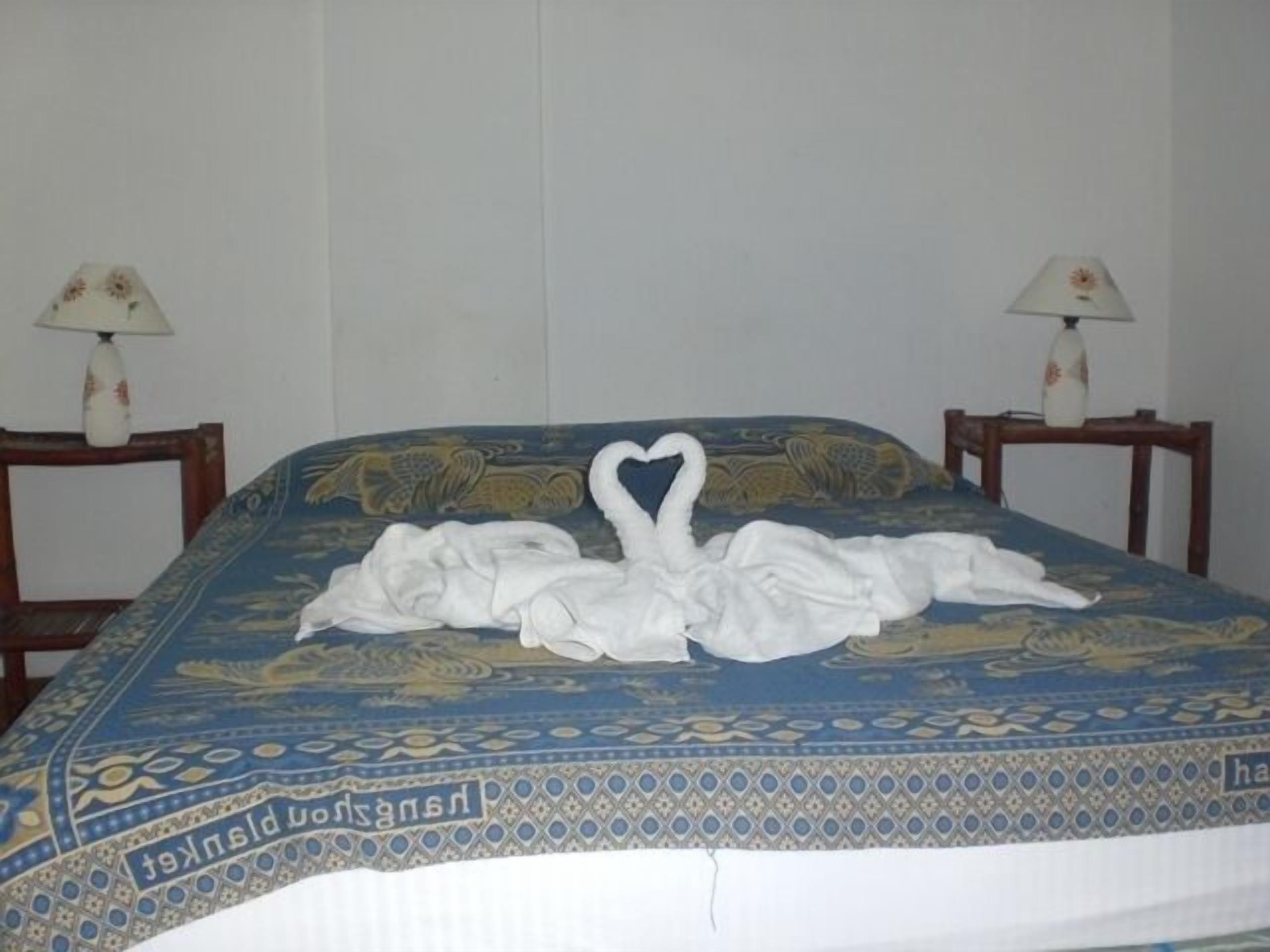 A bed with a blue and gold patterned bedspread, two nightstands with lamps, and a swan and goose towel art on the bed.