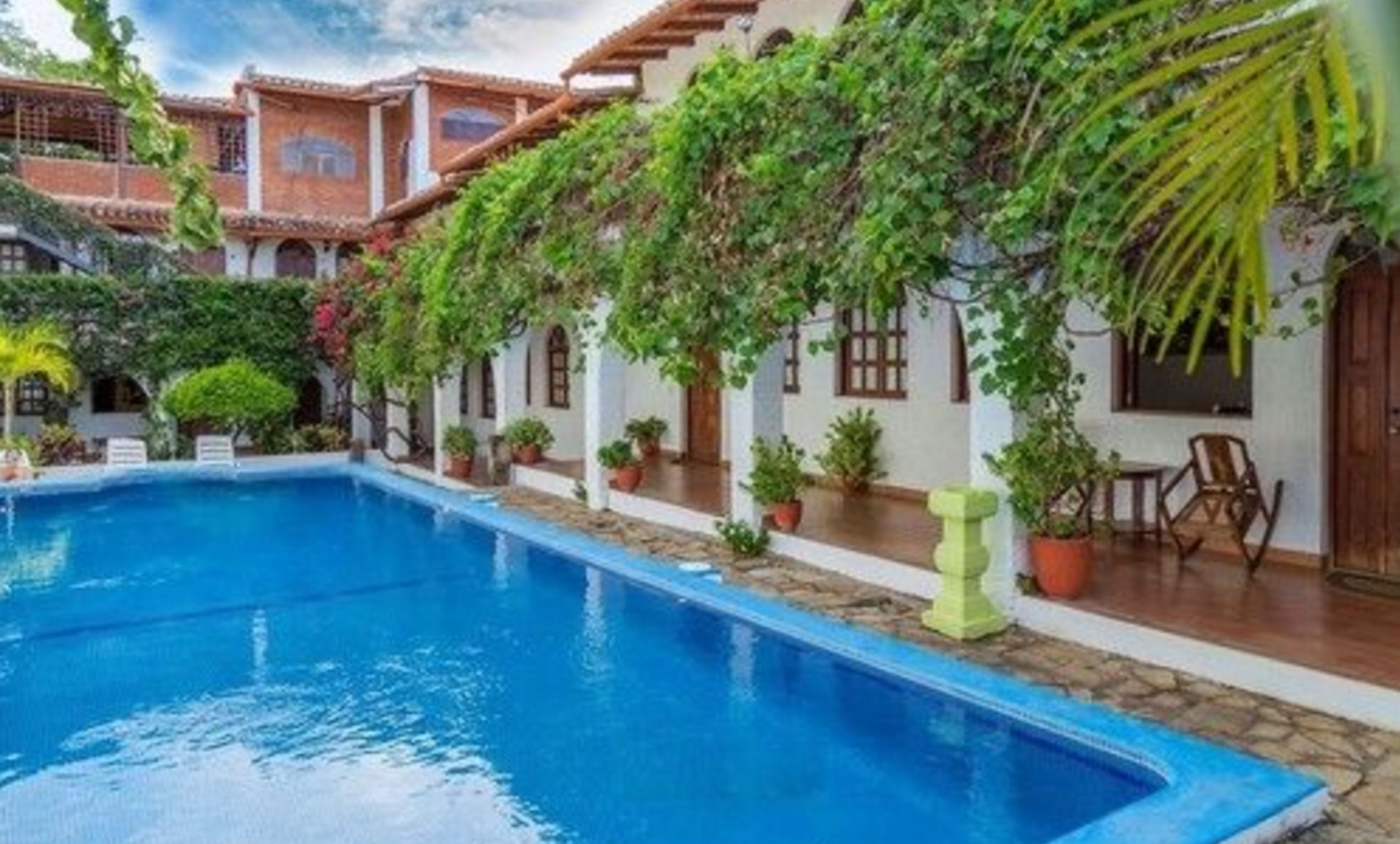 A pool area with a clear blue pool, surrounded by potted plants and a patio with outdoor seating.