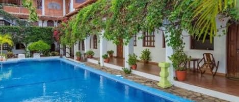 A pool area with a clear blue pool, surrounded by potted plants and a patio with outdoor seating.