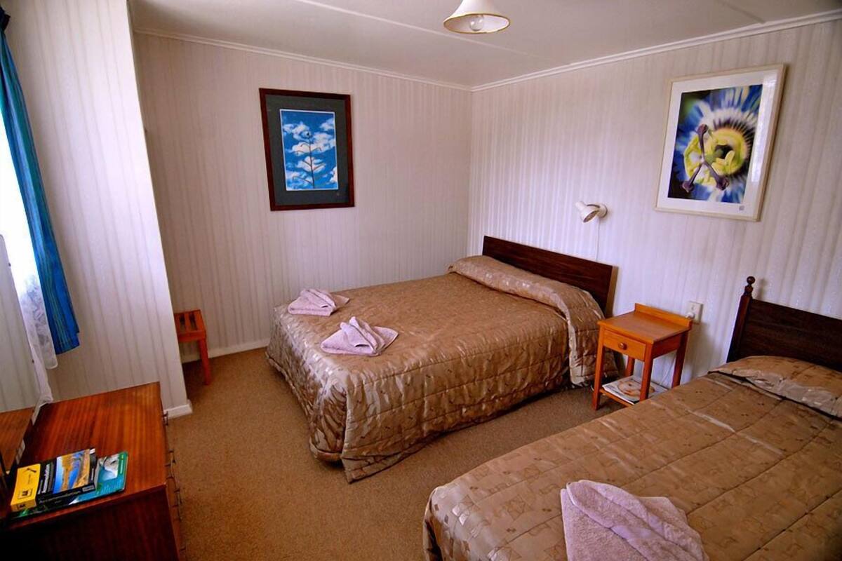 A hotel room with two beds, a wooden nightstand, a small table, and a framed picture on the wall.