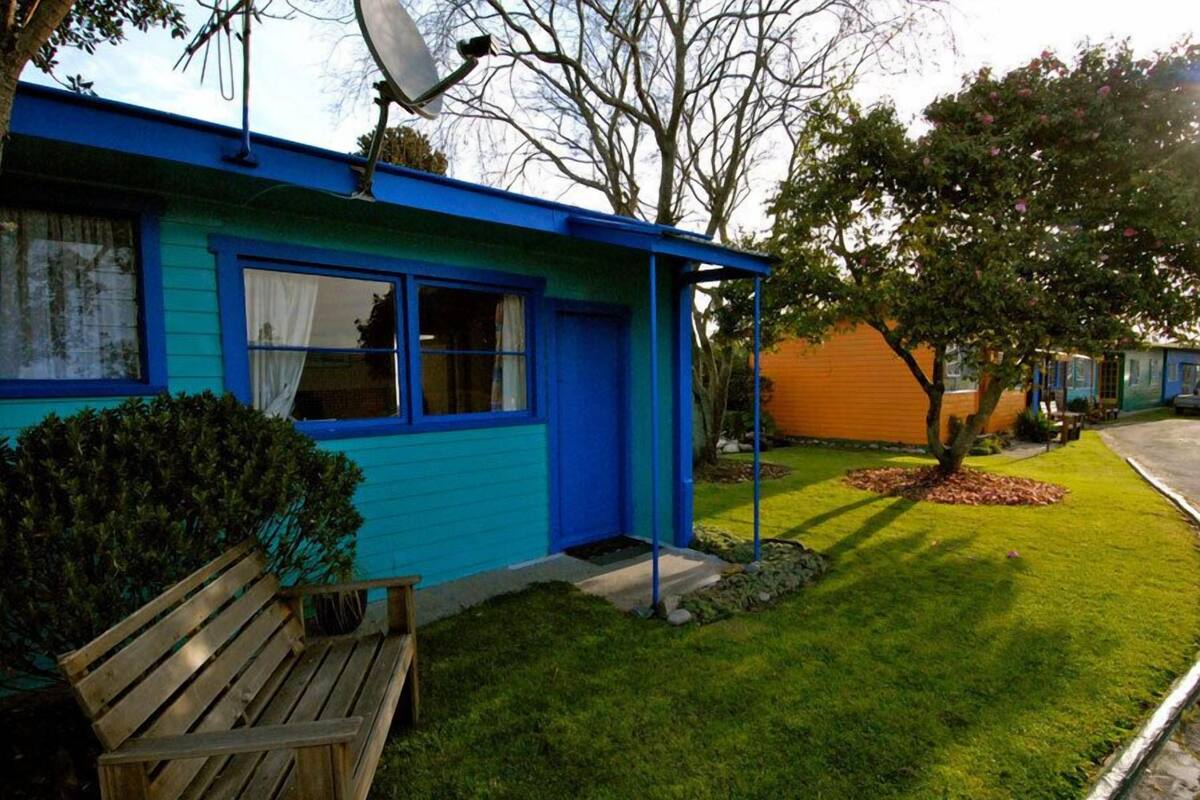 A blue house with a small front yard, a bench, and a tree.